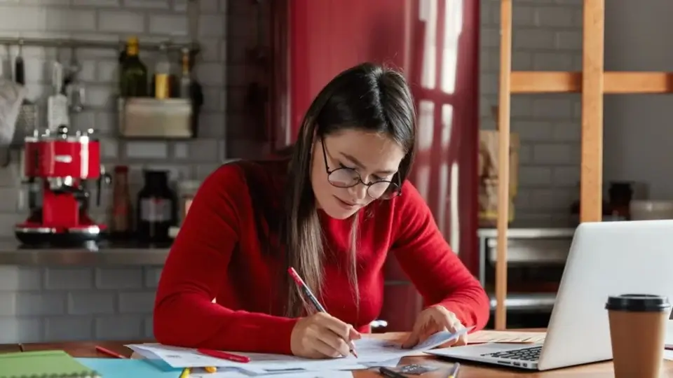 Úvodní obrázek k článku 5 tipů jak se obklopit angličtinou. Článek napsala Ivana Bártková, lektorka angličtiny a majitelka jazykové školy Top English. Na obrázku je žena s brýlemi, sedí a píše.