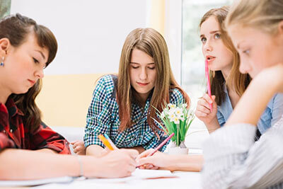 Dospívající děti (teenageři) sedí u stolu a píší v kurzu angličtiny pro teenagery v jazykové škole Top English.